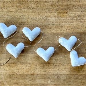 A garland of seven white felt hearts strung together with natural cord.