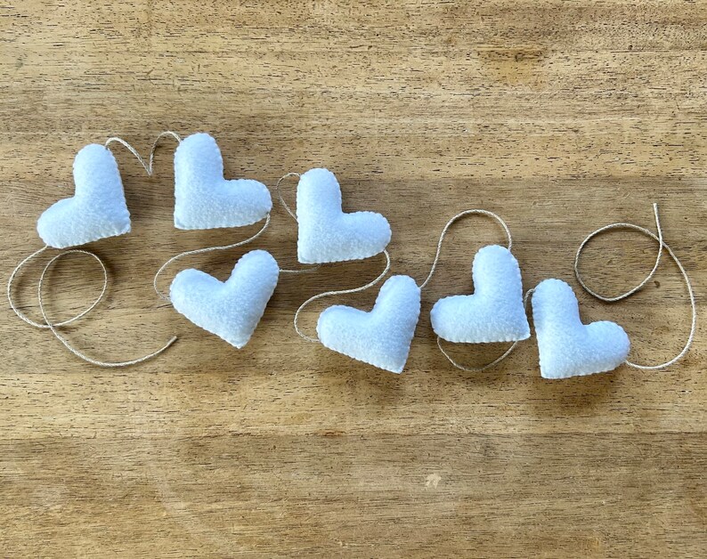 A string of white felt hearts connected with natural cord. The hearts are arranged in a curved line, with the string running through the top of each heart.