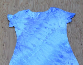 May include: A light blue tie-dye dress with short sleeves, displayed on a wooden surface. The dress has a scoop neck and an A-line shape. The fabric features a swirling pattern of light and dark blue shades.