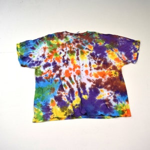 Puede incluir: Una camiseta tie-dye con fondo blanco y una variedad de colores, incluyendo morado, azul, verde, naranja y marrón.