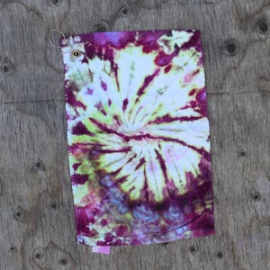 May include: A tie-dye golf towel with a white center and a swirling pattern of pink, purple, green, and yellow.