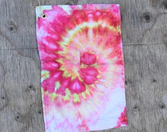 May include: A pink, yellow, and white tie-dye golf towel with a gold metal loop.