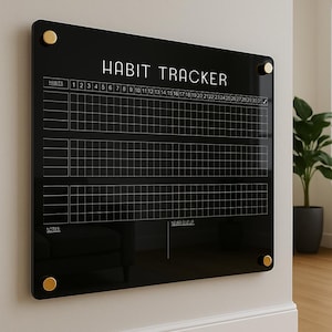 May include: A black acrylic habit tracker with gold fixings. The white text reads "HABIT TRACKER" and includes a grid for tracking habits over 31 days. The bottom of the tracker has the text "NEVER GIVE UP".