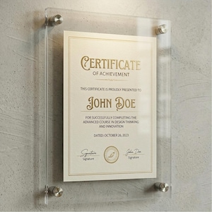 Puede incluir: Un marco de acrílico transparente que muestra un certificado. El certificado, con letras doradas, dice "CERTIFICATE OF ACHIEVEMENT" y se presenta a "JOHN DOE". Con fecha del 26 de octubre de 2023, está asegurado con herrajes plateados contra una pared texturizada.