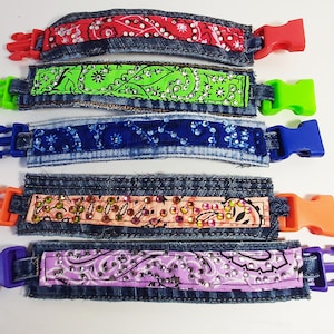 May include: Five colorful denim bracelets with different patterned fabric inserts and plastic clasps. The bracelets are in a row, with the red and green bracelets at the top and the purple bracelet at the bottom.