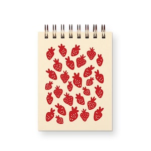 May include: A spiral-bound notepad with a cream-colored cover featuring a pattern of red strawberries. The strawberries are stylized with a simple, hand-drawn aesthetic. The notepad has a metal spiral binding at the top.