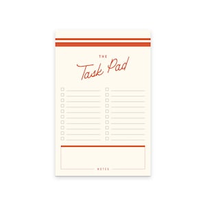 May include: Cream-colored task pad with the words "The Task Pad" in a handwritten style in red. The pad has a grid of checkboxes and lines for writing tasks, with a section for notes at the bottom. Two red stripes are at the top.