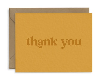 May include: A yellow card with the words "thank you" in a bold, retro font.