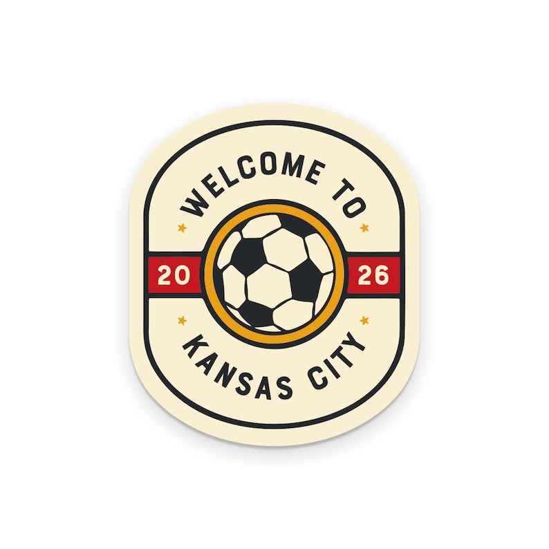 May include: Cream-colored oval sticker with a soccer ball graphic. The sticker features the text "WELCOME TO KANSAS CITY" in a circular design, with the numbers "20" and "26" on red bars. A yellow circle surrounds the soccer ball.