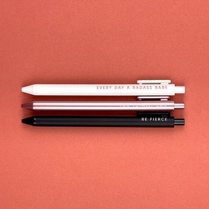 Three pens on a red background. Everyday a badass babe pen (white pen, black ink, red lettering), You totally can pen (rose gold pen, white lettering, black ink), Be Fierce (Black pen, white lettering, black ink)