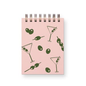 May include: A pink notebook with a spiral binding features a repeating pattern of green olives and martini glasses.