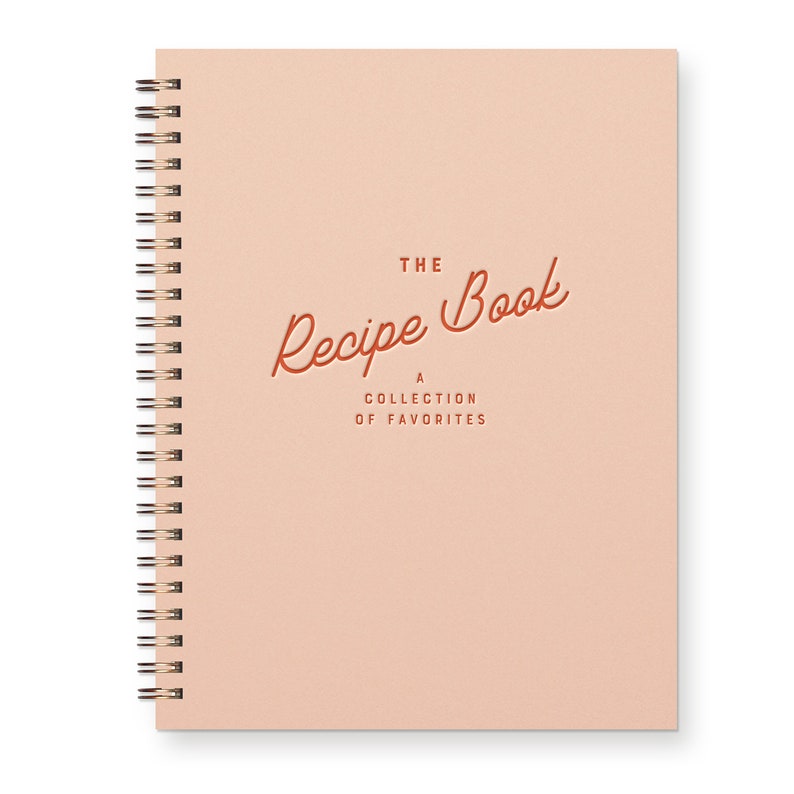 Spiral Bound Keepsake recipe book with a timeless font that reads "The Recipe Book A Collection Of Favorite." The book is pink with red text.
