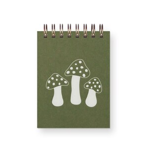 A small, top spiral bound green notebook with three white toadstool mushrooms on it.