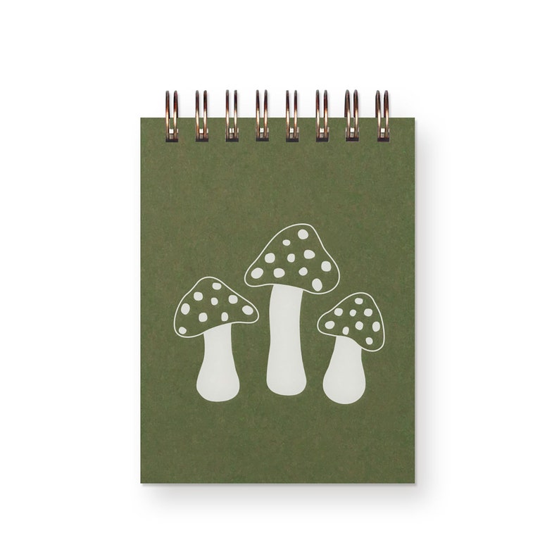 A small, top spiral bound green notebook with three white toadstool mushrooms on it.