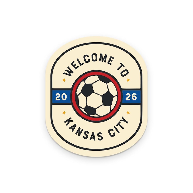 May include: A cream-colored sticker with a soccer ball graphic inside a red circle. The text "WELCOME TO KANSAS CITY 2026" is printed around the soccer ball in a black, bold font. The sticker has a rounded rectangular shape.