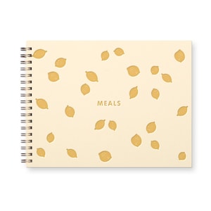 May include: A spiral-bound notebook with a cream-colored cover featuring a pattern of yellow lemons. The word "MEALS" is printed in gold in the center of the cover. The notebook has a silver spiral binding.