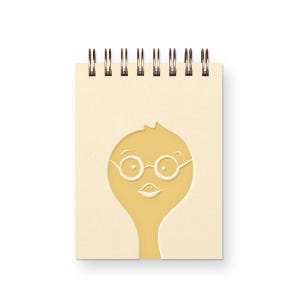 May include: A spiral-bound notepad with a light tan cover featuring a cut-out design of a yellow cartoon character wearing round glasses. The character has a small mouth and a tuft of hair. The spiral binding is bronze-colored.