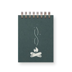 May include: A dark green spiral bound notebook with a white illustration of a campfire with smoke rising from it.