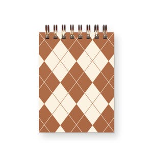 May include: A rectangular spiral-bound notebook featuring a repeating argyle pattern of cream and terracotta brown diamonds. The top edge is secured with a dark metallic wire coil binding, allowing the pages to flip over the top of the cover.