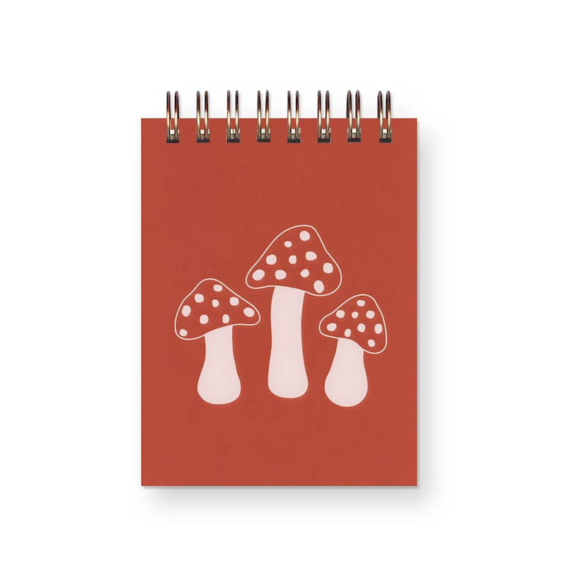 A small, top spiral bound red notebook with three white toadstool mushrooms on it.