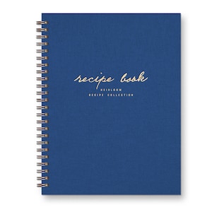 Spiral bound keepsake recipe book with blue linen cover. Gold foil font reads "recipe book heirloom recipe collection."