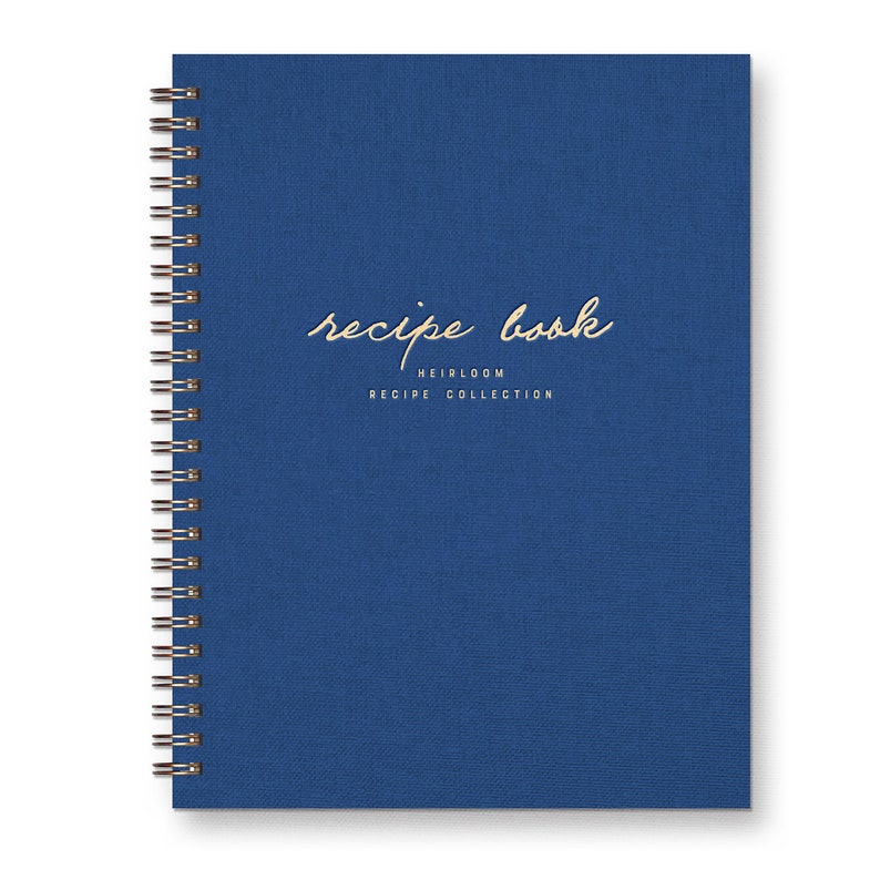 Spiral bound keepsake recipe book with blue linen cover. Gold foil font reads "recipe book heirloom recipe collection."