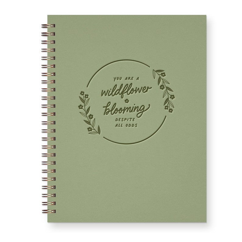 Spiral bound, Aloe green journal with dark green ink design, "You are a wildflower blooming despite all odds". surrounded by a circle with flowers