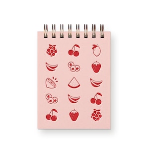 May include: A pink spiral notebook with red fruit illustrations. The illustrations include cherries, lemons, bananas, strawberries, blueberries, raspberries, and watermelon.