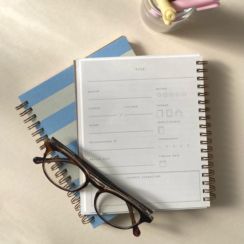 Peut inclure: Un livre blanc avec une couverture ray&eacute;e bleu et blanc. Le livre a une reliure spirale dor&eacute;e et est ouvert &agrave; une page avec un mod&egrave;le de revue de livre. Le mod&egrave;le comprend des champs pour le titre, l'auteur, la note, le format, le nombre de pages, la longueur, l'engagement, la date de la revue, la date de publication et les personnages pr&eacute;f&eacute;r&eacute;s.
