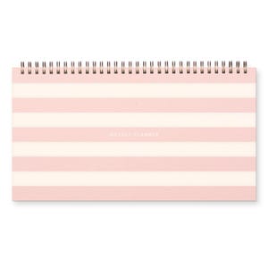 May include: A pink and white striped weekly planner with a black wire binding. The planner has the words "Weekly Planner" printed in black on the front.