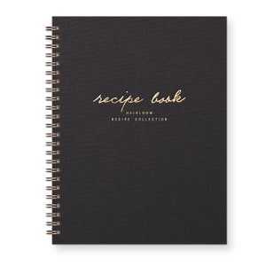Spiral bound keepsake recipe book with black linen cover. Gold foil font reads "recipe book heirloom recipe collection."