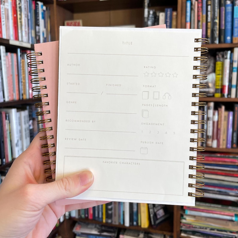 Peut inclure: Un livre blanc avec une reliure spirale dor&eacute;e. Le livre a une page blanche avec des titres pour "Auteur", "Titre", "&Eacute;valuation", "D&eacute;but&eacute;", "Termin&eacute;", "Format", "Genre", "Recommand&eacute; par", "Date de lecture", "Longueur des pages", "Engagement", "Date de publication", et "Personnages pr&eacute;f&eacute;r&eacute;s".