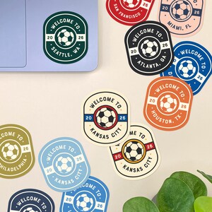 May include: A collection of colorful soccer-themed stickers with the text "WELCOME TO" and various city names, including Seattle, San Francisco, and Miami. Each sticker features a soccer ball and the numbers "20" and "26".