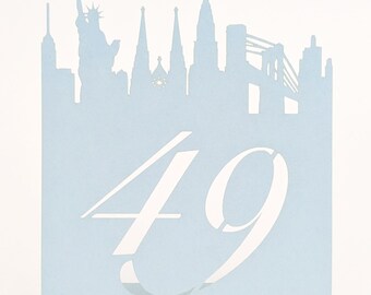 May include: A light blue table number card featuring a New York City skyline silhouette at the top. The number "49" is displayed in white, stylized font. The card is rectangular and stands upright.