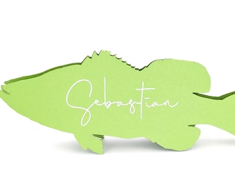May include: A light green fish-shaped place card with the name "Sebastian" in white script. The place card is cut from a single piece of paper and has a simple, clean design, perfect for a nautical or aquatic-themed event.