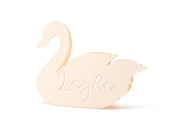 May include: A light beige, swan-shaped cutout made of cardstock or paper. The swan is depicted in profile with its neck curved and wings folded. The name Layla is written across the center of the swan body in a white, cursive script font.