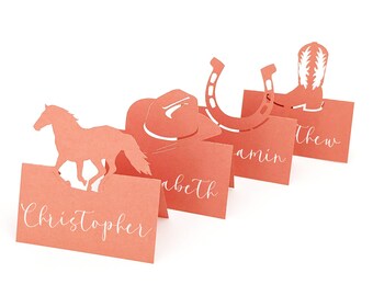 May include: Coral-colored place cards with Western-themed cutouts, including a horse, cowboy hat, horseshoe, and boot. Each card has a name in white script. Perfect for a rustic wedding or event.