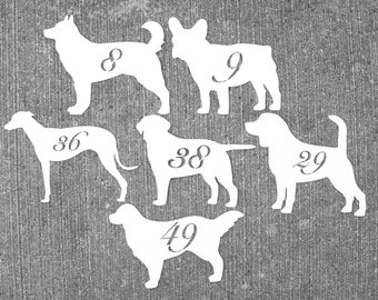 May include: White dog silhouettes with numbers 8, 9, 29, 36, 38, and 49. The dog breeds include a Husky, French Bulldog, Greyhound, Labrador, and Golden Retriever. The cutouts are on a gray concrete surface.