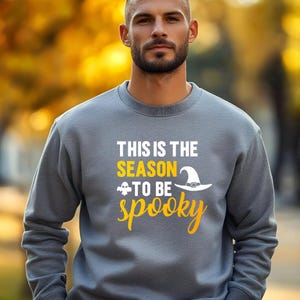 May include: Gray sweatshirt with the text "THIS IS THE SEASON TO BE spooky" in white and yellow. The design includes a witch hat and a ghost. The sweatshirt is a crew neck style.