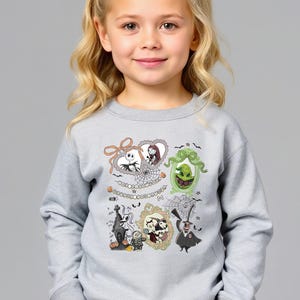 Może przedstawiać: Jasnoszara bluza z nadrukiem postaci z filmu The Nightmare Before Christmas w ramkach. Ramki zawierają Jacka Skellingtona, Sally, Oogie Boogie i inne postacie. Wyprodukowano w USA.