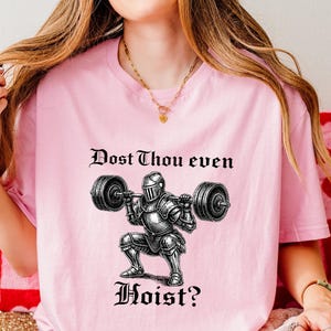 May include: Pink t-shirt with the text "Dost Thou even Hoist?" above a graphic of a knight lifting weights. The shirt also has a small American flag and the words "Made in USA".