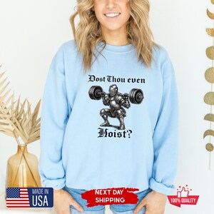 May include: Light blue sweatshirt with the text "Dost Thou even Hoist?" above a graphic of a knight lifting weights. The sweatshirt has a crew neck and long sleeves. Made in the USA.