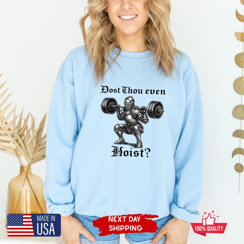May include: Light blue sweatshirt with the text "Dost Thou even Hoist?" above a graphic of a knight lifting weights. The sweatshirt has a crew neck and long sleeves. Made in the USA.