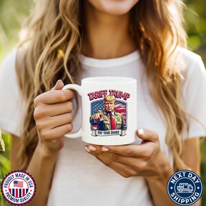May include: White ceramic coffee mug with a colorful illustration of Donald Trump with the text "Tariff Trump Pay Your Share" on the front.