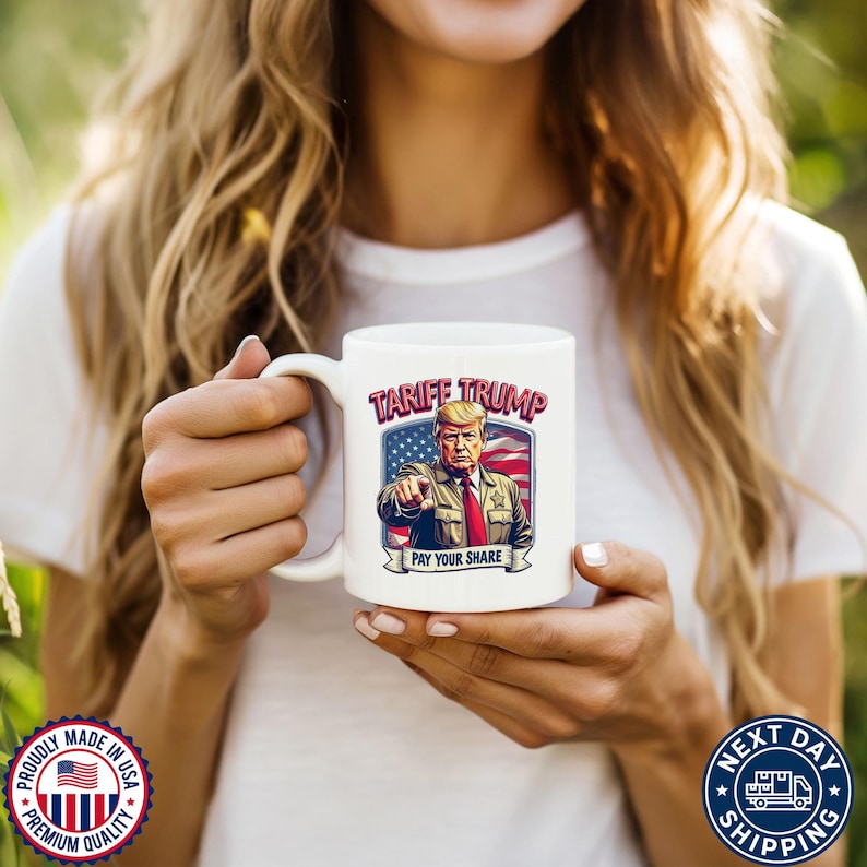 May include: White ceramic coffee mug with a colorful illustration of Donald Trump with the text "Tariff Trump Pay Your Share" on the front.