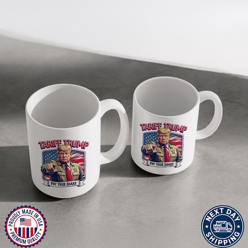 May include: Two white ceramic mugs with a graphic of Donald Trump on them. The graphic says "Tariff Trump" and "Pay Your Share". The mugs are on a white surface.