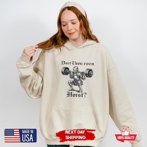 May include: A beige hoodie with a front graphic of a knight lifting weights, with the text "Dost Thou even Hoist?". The hoodie has a kangaroo pocket and a drawstring hood. The image also includes a "Made in USA" graphic.
