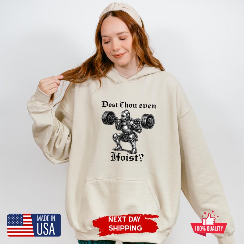 May include: A beige hoodie with a front graphic of a knight lifting weights, with the text "Dost Thou even Hoist?". The hoodie has a kangaroo pocket and a drawstring hood. The image also includes a "Made in USA" graphic.