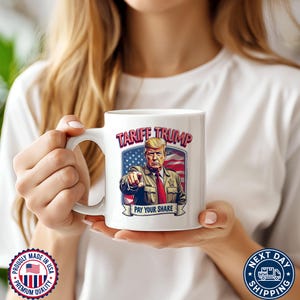 May include: White ceramic coffee mug with a graphic of Donald Trump in front of an American flag. The text "Tariff Trump" and "Pay Your Share" are printed on the mug.