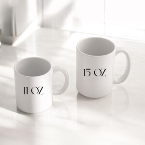 May include: Two white ceramic mugs with black text. The smaller mug is labeled "11 OZ" and the larger mug is labeled "15 OZ".